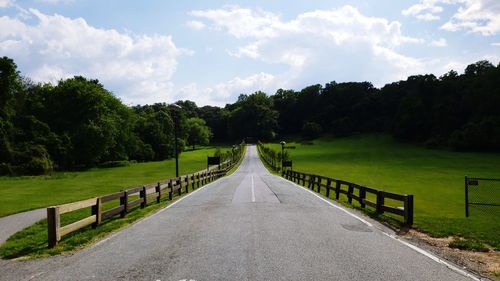 Empty road along trees and plants against sky