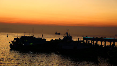 Silhouette boats in sea against orange sky