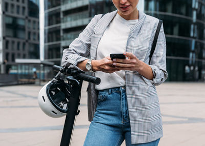 Cropped shot of businesswoman leaning on handlebar of electric scooter using an app for rent	