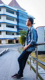 Young man looking away while sitting on railing in city