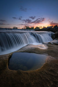 Scenic view of waterfall against sky during sunset