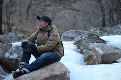 Full length of man sitting on rock in snow
