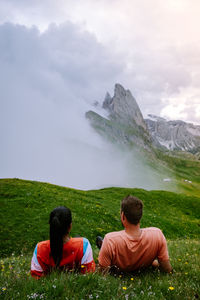 Rear view of people sitting on land against sky