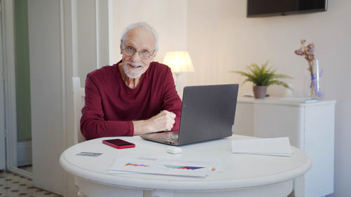 Portrait of senior man sitting by laptop at home