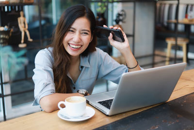 Portrait of a young woman using phone while sitting on table