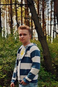 Portrait of young man standing against trees in forest