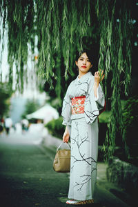 Young woman standing by tree trunk