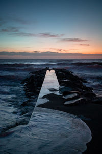 Pier leading towards sea against sky during sunset