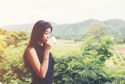 Beautiful young woman drinking water from plant