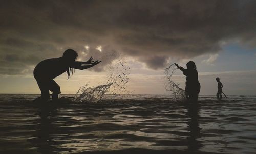 Silhouette women splashing water in sea against sky