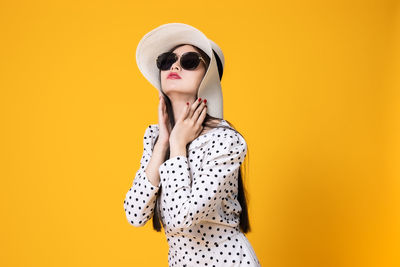 Young woman wearing sunglasses standing against yellow background
