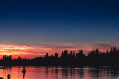 Silhouette trees by lake against sky during sunset