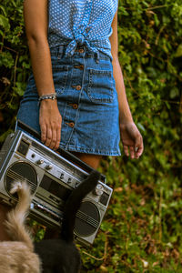 Low section of woman holding retro radio standing outdoors with cats and tails 