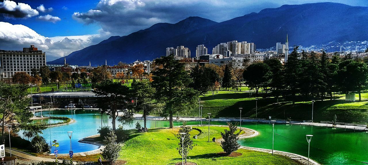 architecture, built structure, building exterior, tree, water, city, river, sky, mountain, cityscape, green color, reflection, lake, growth, waterfront, bridge - man made structure, tower, travel destinations, nature, skyscraper