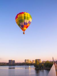 Hot air balloon flying over river against sky during sunset