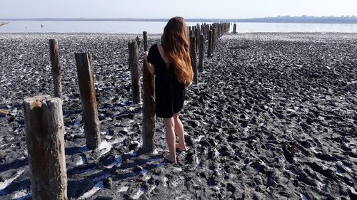 Rear view of woman standing at beach against sky