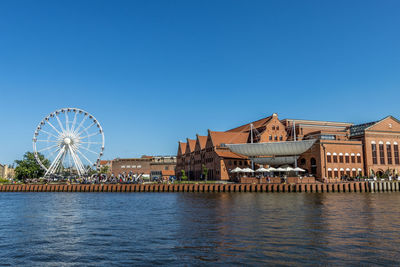 Ferris wheel by river against buildings