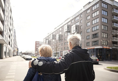 Rear view of senior couple walking on city street against clear sky