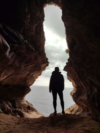 Single person standing inside a cave with sea and sky view