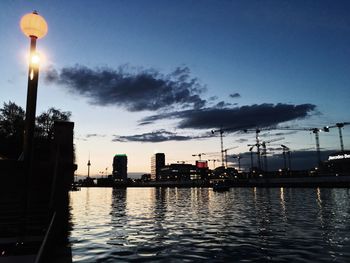 Silhouette city by river against sky at night