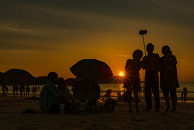 People at beach against sky during sunset
