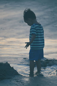 Boy standing on shore at beach against sky