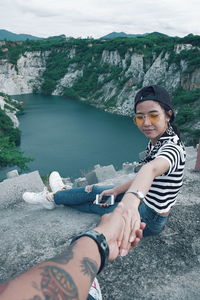 Cropped hand of man holding girlfriend sitting on rock formation