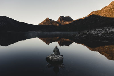 Rear view of person on rock amidst calm lake against mountain