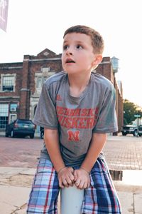 Boy looking away while sitting on bollard against sky