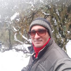 Portrait of young man wearing sunglasses against trees during winter
