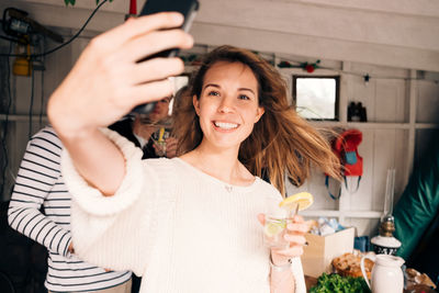 Young woman taking selfie on smart phone with friends in cottage