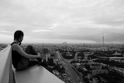 Rear view of man sitting on buildings in city against sky