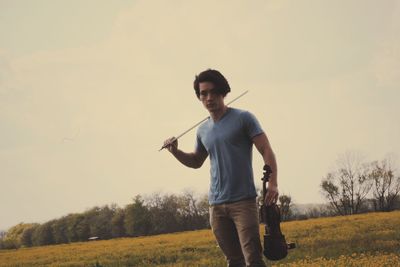 Man holding violin while standing on field against sky