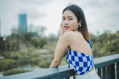 Portrait of young woman standing against railing