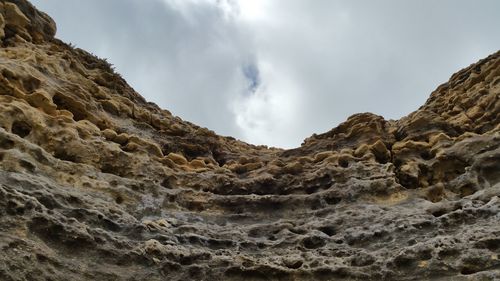 Low angle view of eroded rocks against cloudy sky