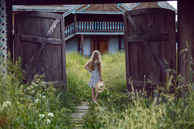 Blonde village girl with long hair stands in a wooden gate in the village in summer