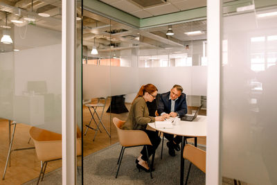 Sales executives discussing over business plans while sitting at work place seen through doorway