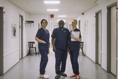 Portrait of smiling male and female medical staff standing together at corridor in hospital