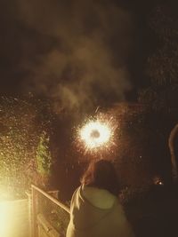 Rear view of woman standing in illuminated park against sky at night