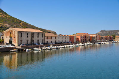 Buildings by canal against clear blue sky