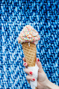 Cropped hand of woman holding sprinkles ice cream cone against blue wall