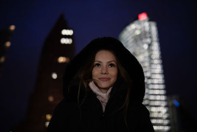 Portrait of beautiful woman standing against city at night