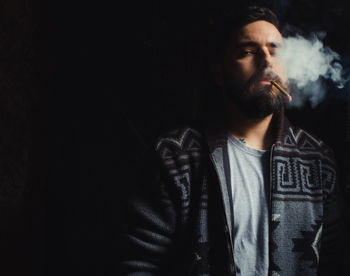 Young man smoking cigarette against black background