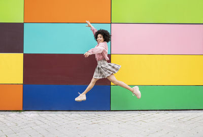 Side view of woman jumping against wall