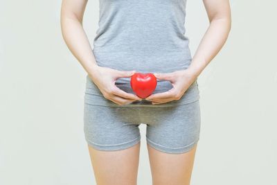 Midsection of woman holding heart shape over white background