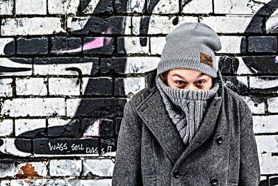 Portrait of man covering face with warm clothing while standing against wall