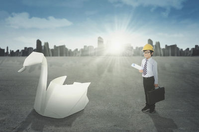 Digital composite image of boy with suitcase standing on road against sky in city during sunny day