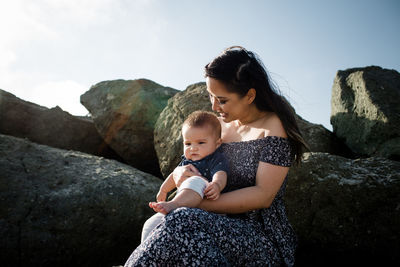 Portrait of mother and son on rock against sky