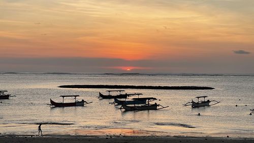 Fishing boats in sea against sky during sunset