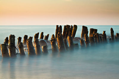 Wooden posts on sea against sky during sunset